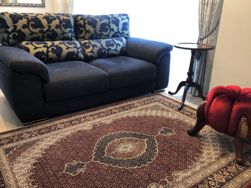 ダークブルーのソファにスツールと絨毯の赤色でメリハリの効いたインテリア